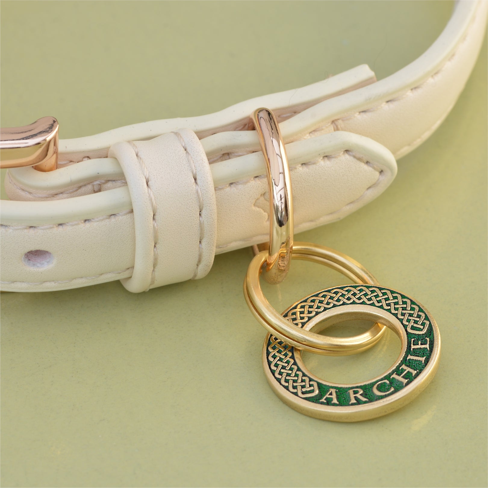 Hoop-shaped brass ID tag with engraved Celtic pattern, handmade in the UK. Suitable for dogs, cats, and horse bridles. Shown attached to a collar for display.