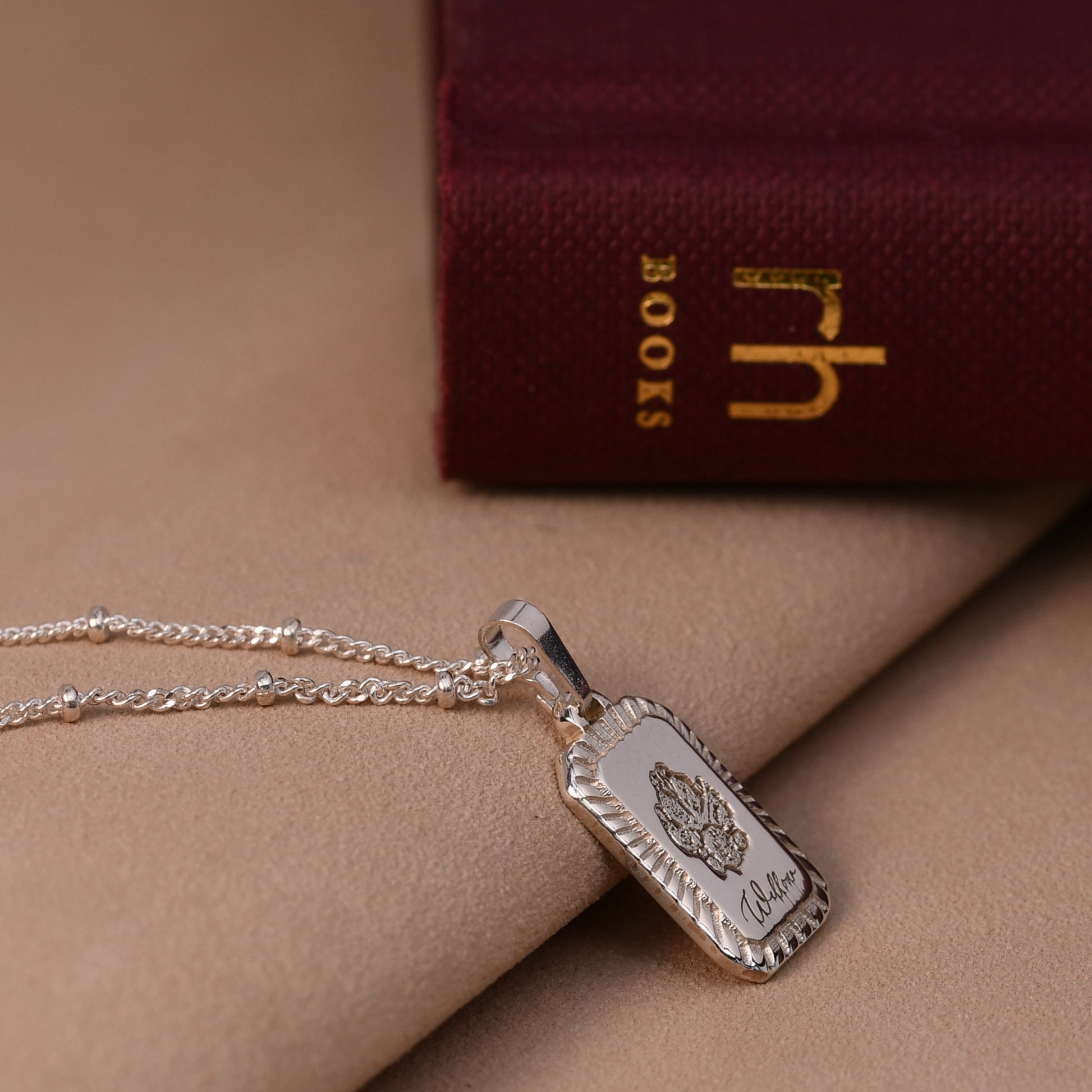 Silver necklace with a tag on a beige surface with a red book in the background