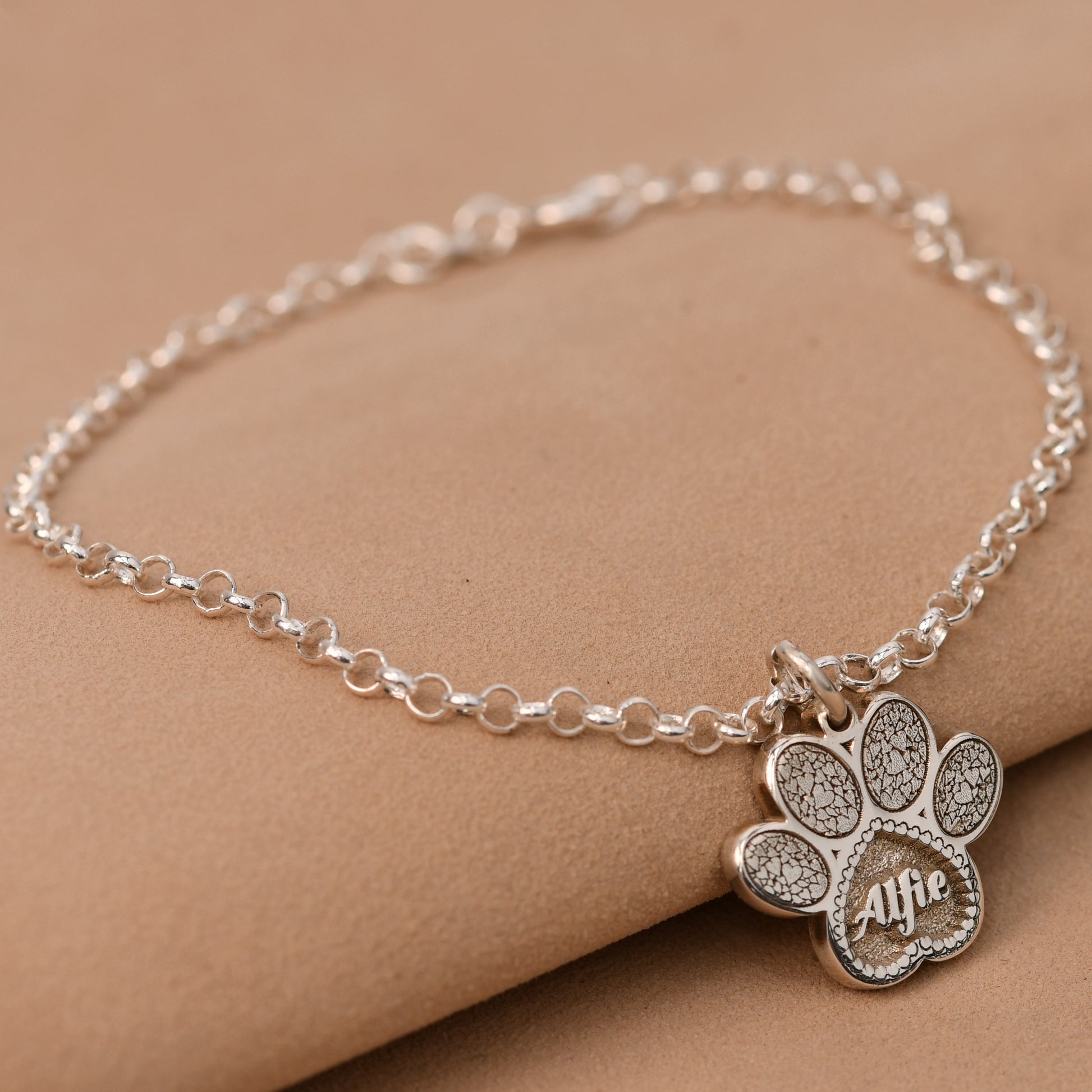 Silver paw print bracelet with 'Ally' on a beige surface
