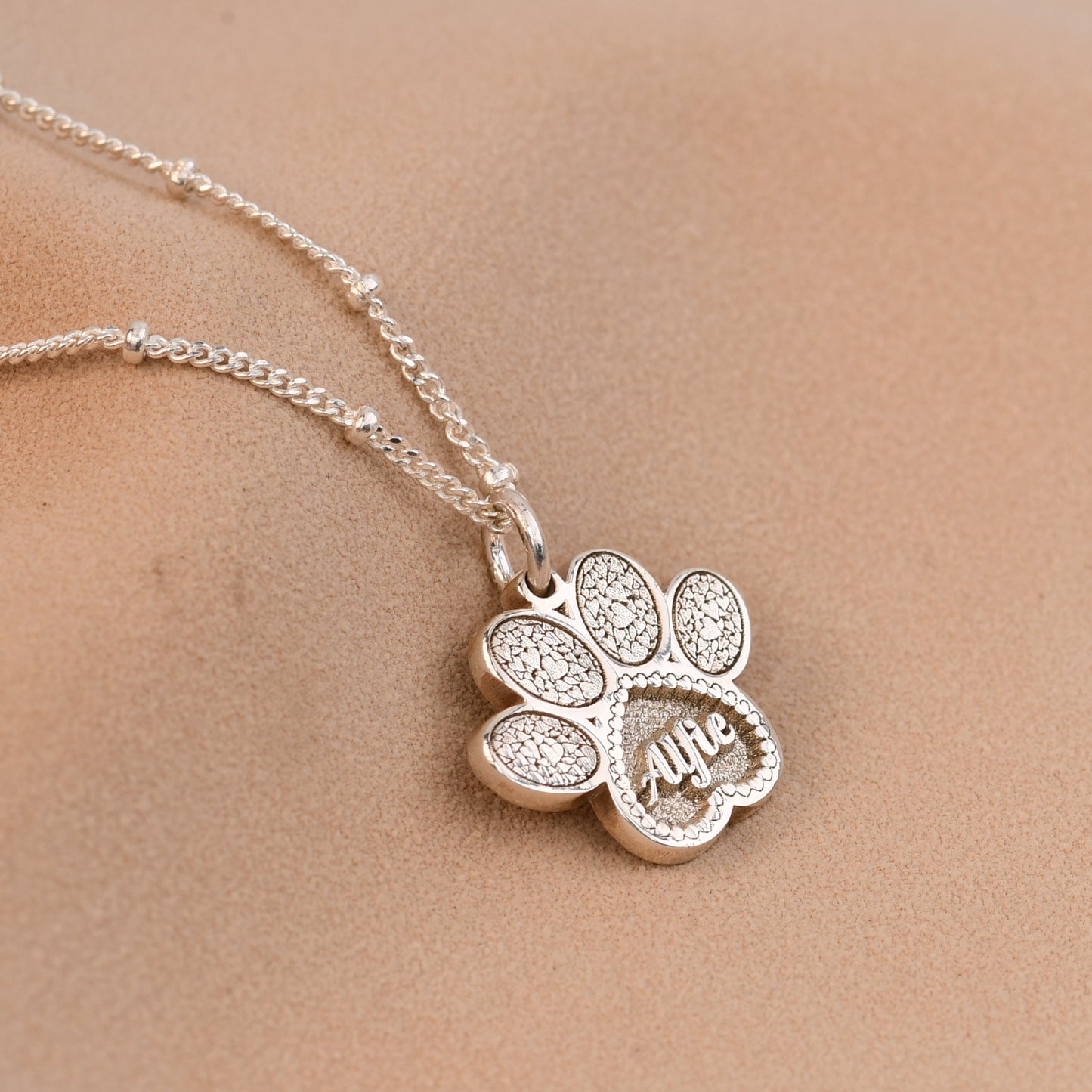 Silver necklace with a paw-shaped pendant on a beige background