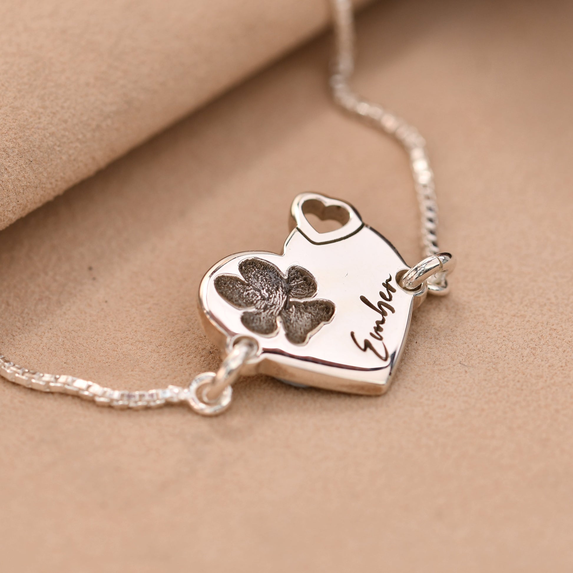 Silver necklace with a heart-shaped pendant featuring paw prints and engraved text on a beige background