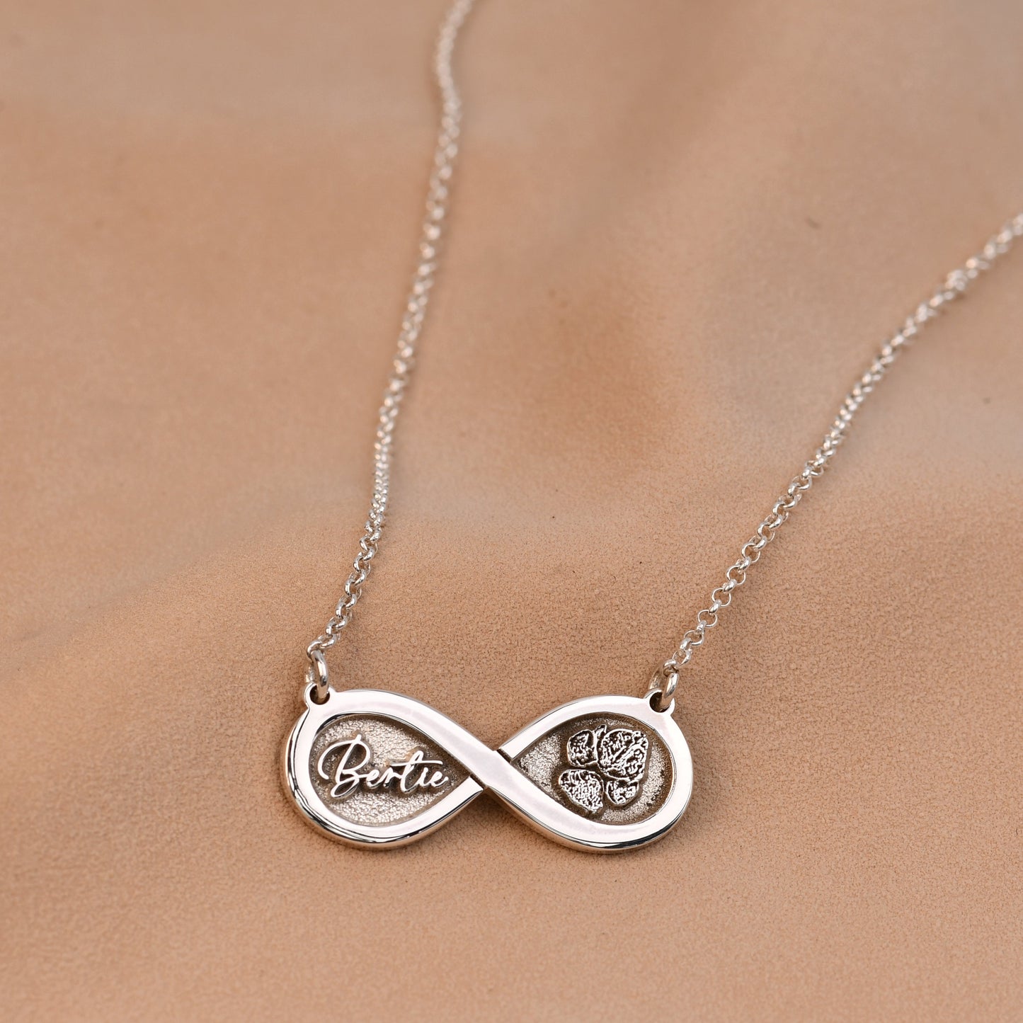 Silver infinity necklace with engraved name on a blurred background