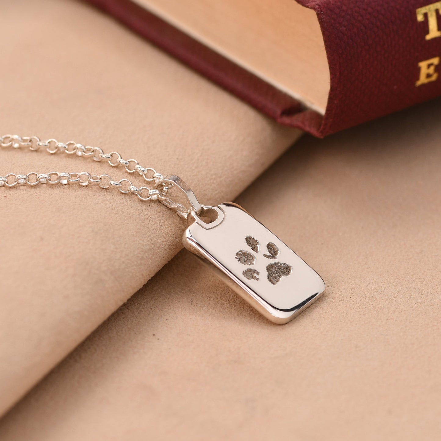 Silver necklace with a dog tag featuring paw prints on a beige surface.