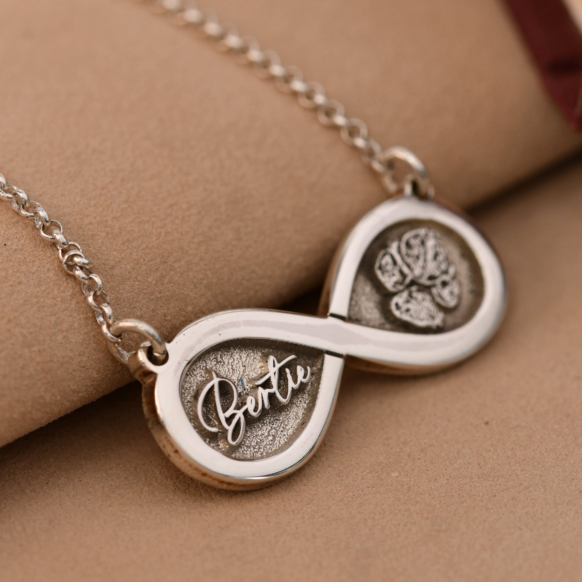 Silver necklace with paw print and 'Bella' engraving on a beige surface