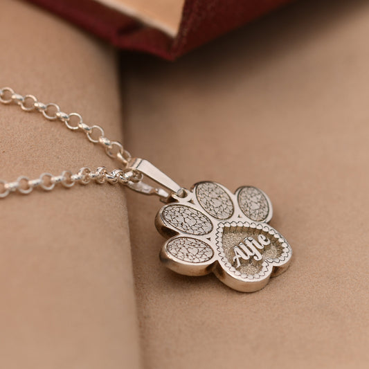 Silver paw-shaped pendant necklace with 'Alfie' engraved on a beige surface